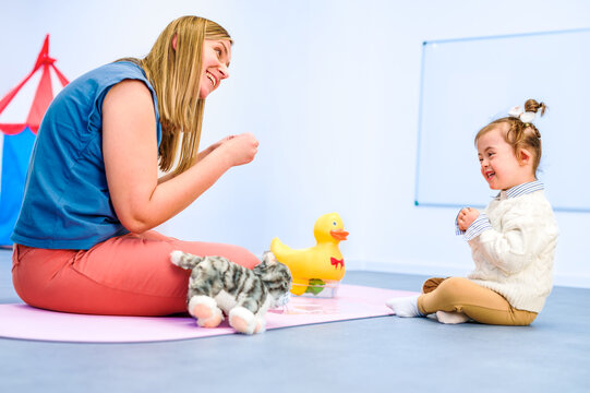 Nonverbal child with Down syndrome learning baby sign language with the help of a speech therapist. Child therapy, neurodiversity, learning difficulty, developmental disability.