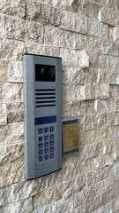 Modern intercom and access control system mounted on a textured stone wall. Features a camera, keypad, and contactless card reader for secure entry. Ideal for residential and commercial buildings.