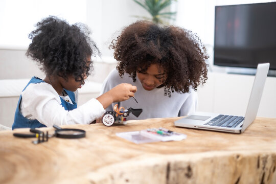 African loving mother and daughter team up for a fun robotics project, exploring hands-on STEM activities that inspire creativity, fostering problem-solving. Mom teaching girl for building robot.