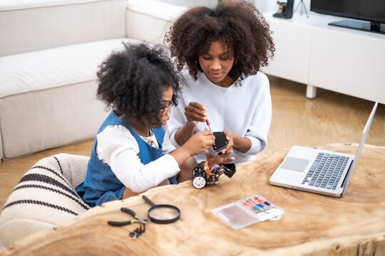 African loving mother and daughter team up for fun robotics project, exploring hands-on STEM activities that inspire creativity, fostering problem-solving. Mom teaches her girl for building robot.