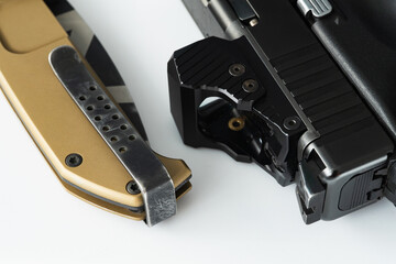 Modern red dot sight on a pistol and tactical folding knife, macro photo.