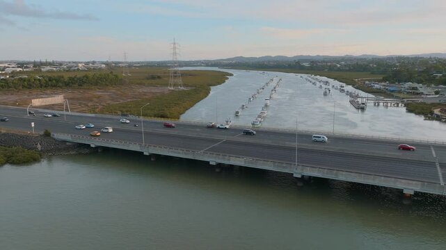 Cars travel across a bridge over the Whau river in Auckland, New Zealand. Boats are docked along the river. The bridge connects the city to the surrounding suburbs.