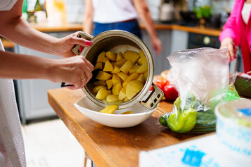 Women's hands pour boiled potatoes from the pan into a bowl. 