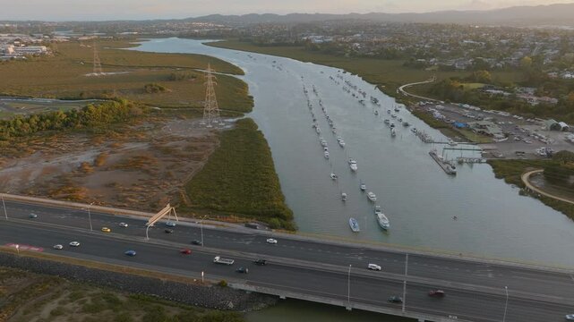 Aerial view of boats moored in the Whau River, Auckland, New Zealand. Cars travel along the bridge. The scene shows transportation and recreation.