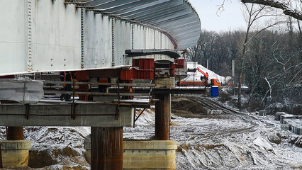 Naklejka premium Construction of a new automobile bridge across the river, on a sunny winter day