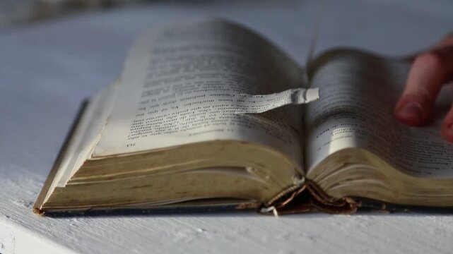 Detailed view of an old book as pages are being flipped and removed by a person's hands