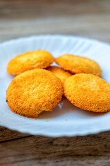 Five golden coconut cookies on a white plate, close-up. Rustic wooden table background. Natural light highlights texture. Simple, appetizing.