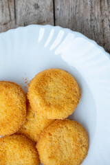 Close-up of golden coconut cookies on a white plate, partial view. Rustic wooden table background. Natural light highlights texture.  Minimalist composition.