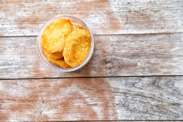 Golden coconut cookies fill a clear container, sitting on a rustic wooden surface with visible grain