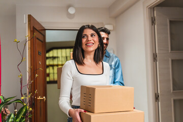 Happy couple carrying boxes entering new home