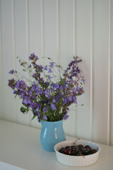 A bouquet of wildflowers in a vase on a white table and charries in bowl
