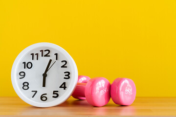 Time for exercising alarm clock and dumbbell with yellow background, sport and healthy concept
