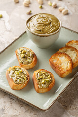 Pistachio butter in bowl with toast on plate raw pistachios closeup on the table. Vertical