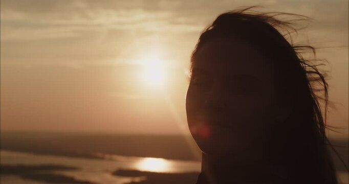 Young woman watching golden sunset over water at dusk