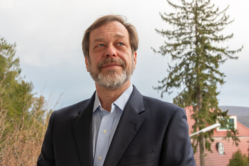 A bearded man in a suit smiles against the backdrop of nature, creating an atmosphere of positivity.