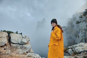 A woman in a yellow raincoat standing on top of a misty mountain, enjoying the beauty of nature