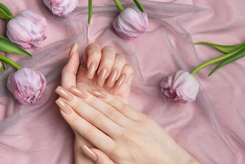 Woman showing nude manicure on pink background with tulips