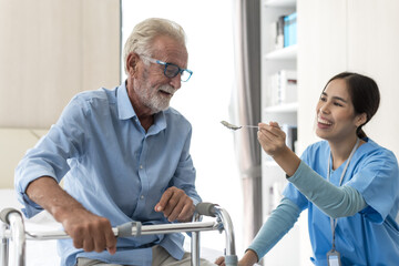 Friendly Asian female nurse feeding food to elderly retirement man for treatment and rehabilitation...