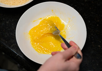 Female hands beat eggs with fork in a bowl, homemade schnitzel cooking process closeup