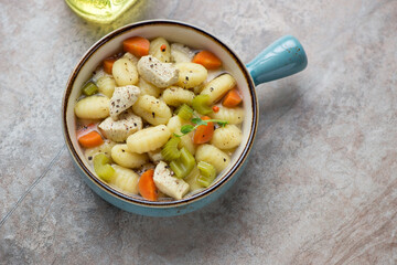 Turquoise serving bowl with chicken gnocchi soup on a brown granite background, horizontal shot, elevated view