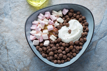 Bowl with chocolate balls, marshmallows and greek yogurt on a blue and beige stone background, horizontal shot, elevated view