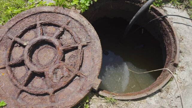 pumping dirty water from a septic tank, open cesspool with a rusty hatch and dirty water sewage, pumping out sewage