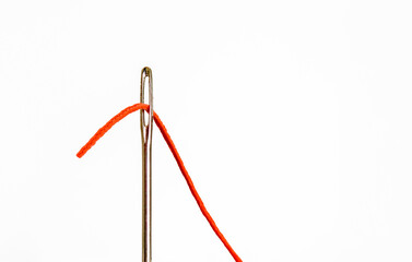 close up image of a large eyed sewing needle with orange cotton being threaded