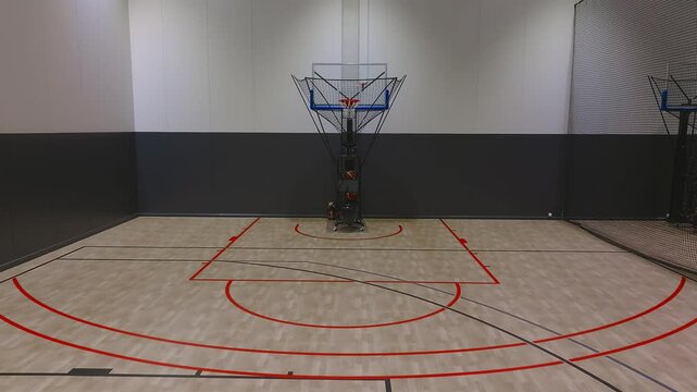 A basketball moves through the air and passes through a hoop with a clear backboard and netted return system in an indoor practice court.