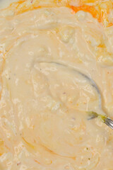 A close-up shot of a creamy mixture of sour cream and egg, showing its texture and a spoon resting inside