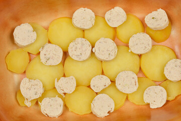 A top-down shot of peeled, boiled potato slices and sausage slices arranged in a baking dish