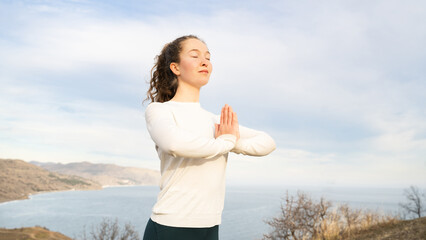 A young woman holding hands in namaste. Girl practicing gratitude meditation at sunrise. Female...