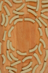 A top-down view of scattered homemade spinach pasta tubes on a wooden surface, arranged to form a...