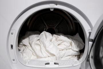 White bedsheets in modern tumble dryer close up laundry scene