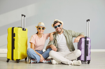 Happy newlywed couple of tourists with suitcases packed, wheel luggage in summer beach wear hat,...