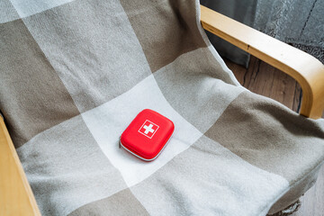 A vibrant red first aid kit is positioned neatly on a chair that is draped with a cozy plaid...