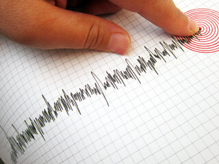 Seismograph and earthquake. A hand pointing at a seismograph recording the seismic activity of an...
