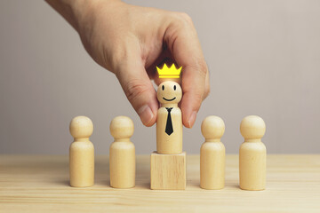 Concept of successful corporate leader. Hand holding wooden block placed on pedestal with crown...