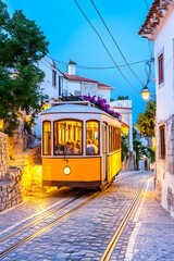 Obraz premium Charming vintage tram ascends a cobblestone hill at twilight, passing whitewashed buildings