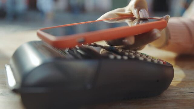 Girl cafe customer applying NFC cellphone to make fast wireless payment. Close-up woman paying for meal order with NFC e-money technology.