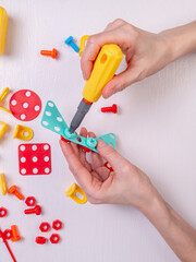 Hands tightening a nut with a screwdriver on a children's plastic construction set at a table, top view