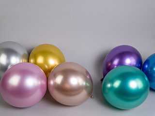 Multicolored metallic balloons lie on a gray background, with space for text