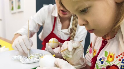 Mother and daughter at the table in traditional Ukrainian costumes painting eggs for Easter