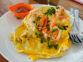 Top view of steamed rice topped with creamy egg sauce and large cooked shrimp on white plate on wooden table.
