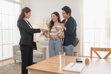 Estate agent hands house keys to the client. Asian woman realtor gives keys to the couple buyer...