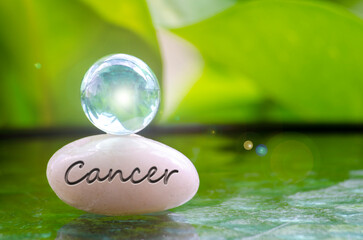 Cancer text engraved on Zen stone with shining glass marble on top. Zodiac concept