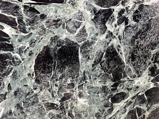 Natural black and white marble slab pattern with golden brown color shades. Black honed marble with wavy white veins, rough stone texture. Minerals seamless background texture.