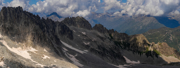 Obraz premium A wide panoramic shot capturing the rugged mountain range with patches of snow and rocky terrain, under a partly cloudy sky.