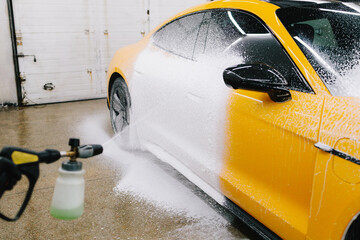 Application of soapy foam with a water gun for sports car cleaning at the service. Worker sprays...