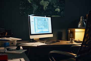 Illuminated modern office setup featuring digital plans on large screen with scattered documents, folders, and equipment on desk creating a busy work environment