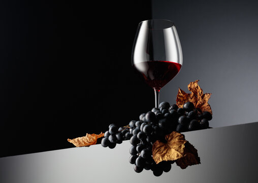 Glass of red wine and blue grapes with dried up vine leaves.